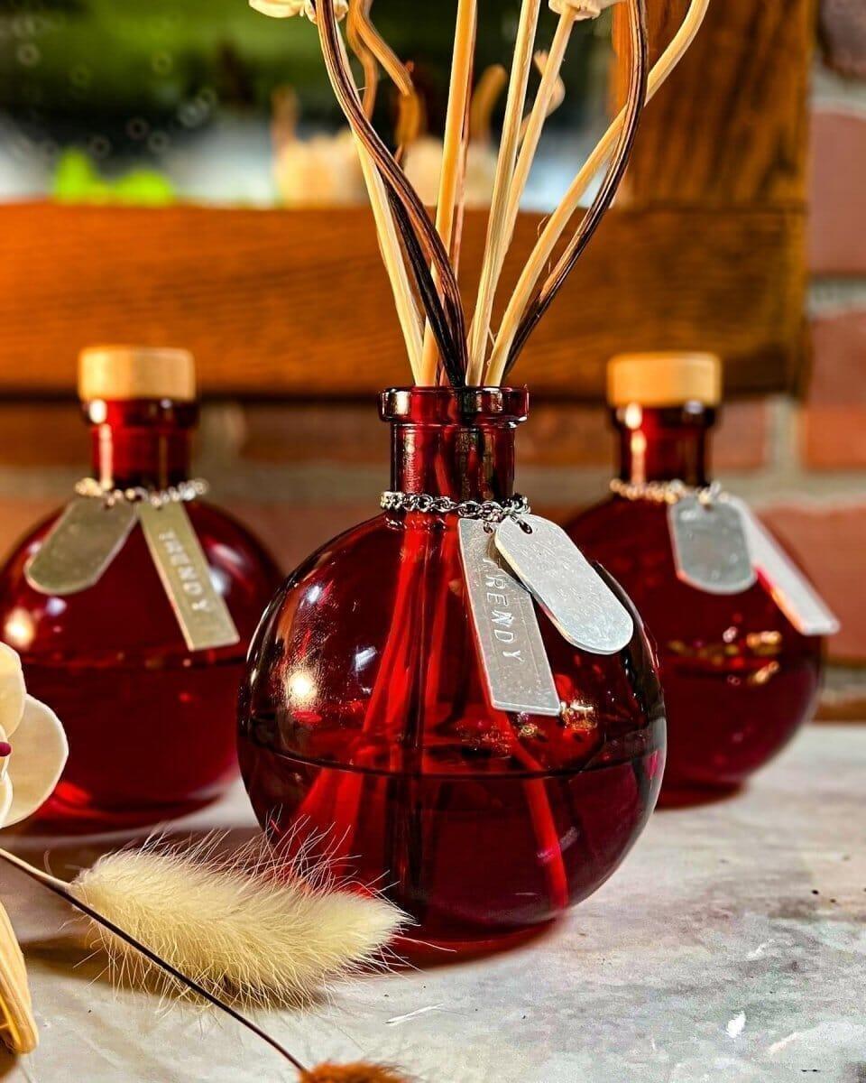 Red glass vases with wooden corks and tags, holding dried ornamental stems on a table.
