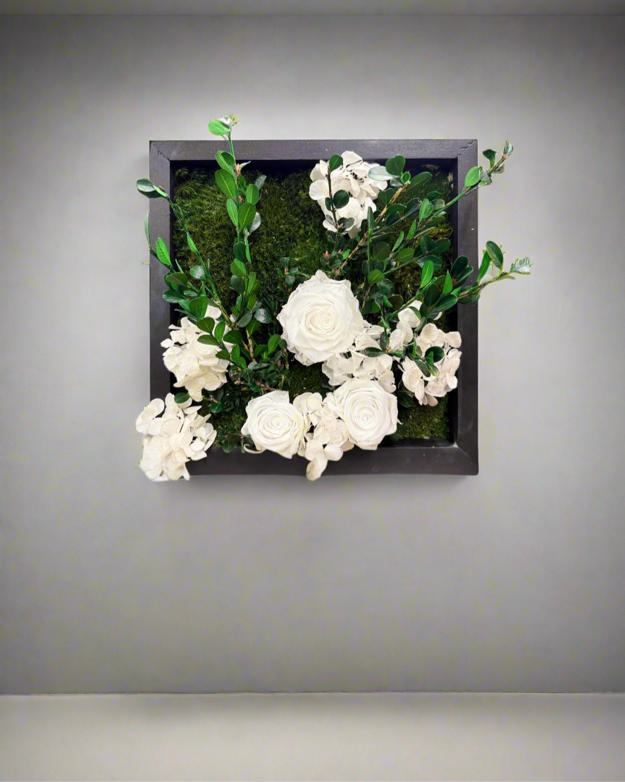 This handcrafted botanical wall art features preserved boxwood, mood moss, delicate preserved white roses, and soft faux hydrangeas, all beautifully arranged in a solid wood frame.