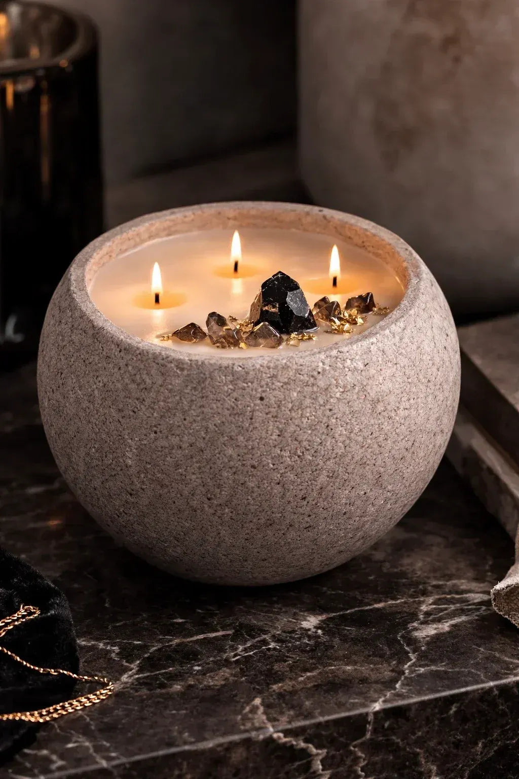 Concrete vessel candle with black obsidian and smoky quartz on a natural stone countertop
